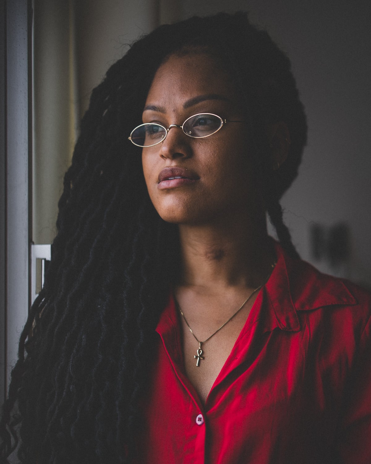 Portrait of Naira Santa Rita wearing a red shirt and glasses.