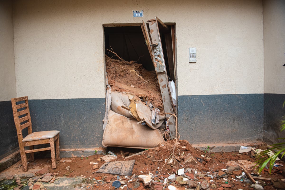 Mud pours through a doorway in an apartment room. The door has broken off its hinges and the dirt reaches almost as high as the door. 