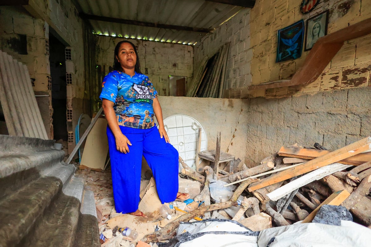 Eduarda Patrícia stands in a room filled with debris, broken planks of wood and furniture.