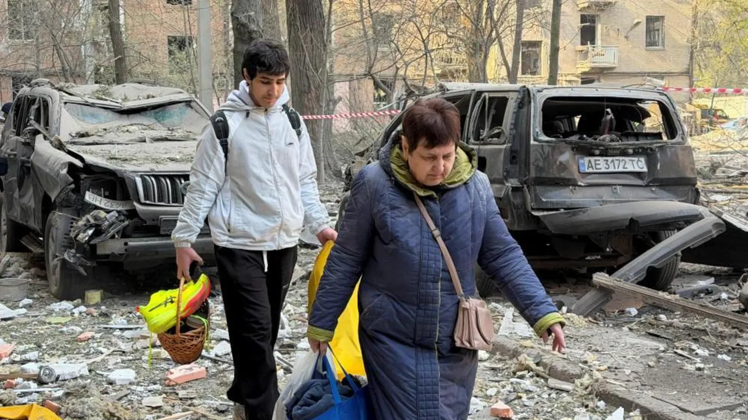  A man and woman carry bags past damaged vehicles as they evacuate following a Russian strike in Ukraine 