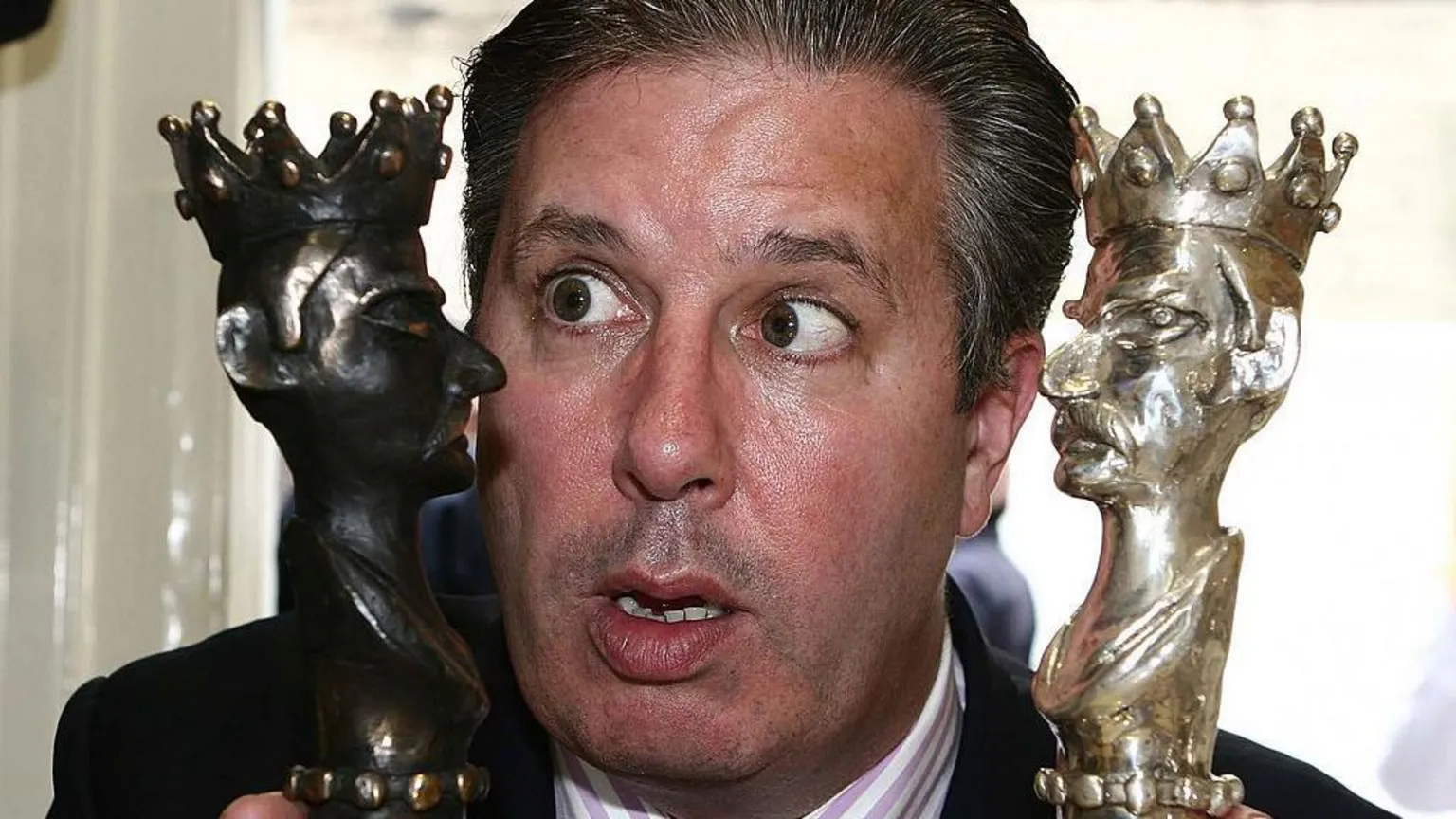  A man holding to awards close to his face, he has black/greyish hair