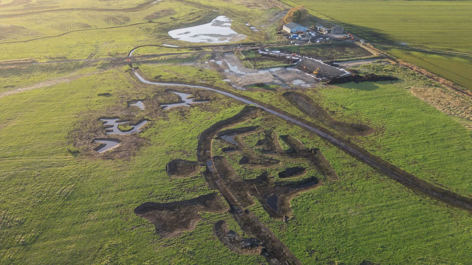 Holly Wilkinson An aerial view of a flat landscape with a large pond and other rivulets nearby. Some agricultural buildings can be seen on the upper right of the image.