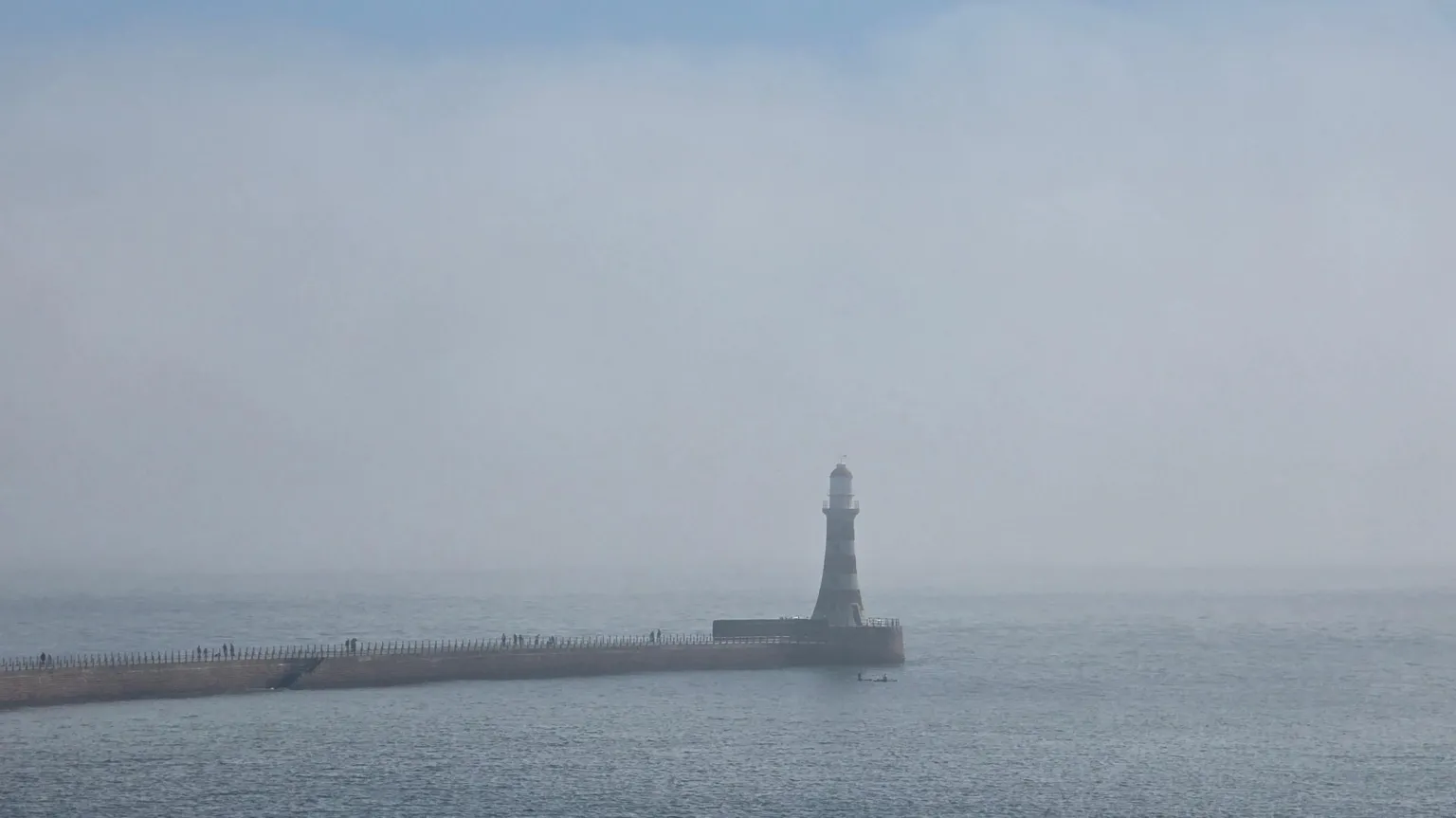 Gill Helps The pier in Sunderland with the lighthouse on the end is covered in mist. The sea is mostly flat and the tone of the sky is a cold grey-blue.
