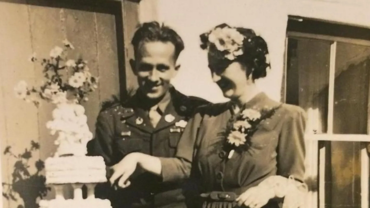 Hans Obma An old black and white photograph from the 1930s shows and man and woman cutting a white tiered cake on their wedding day. 
