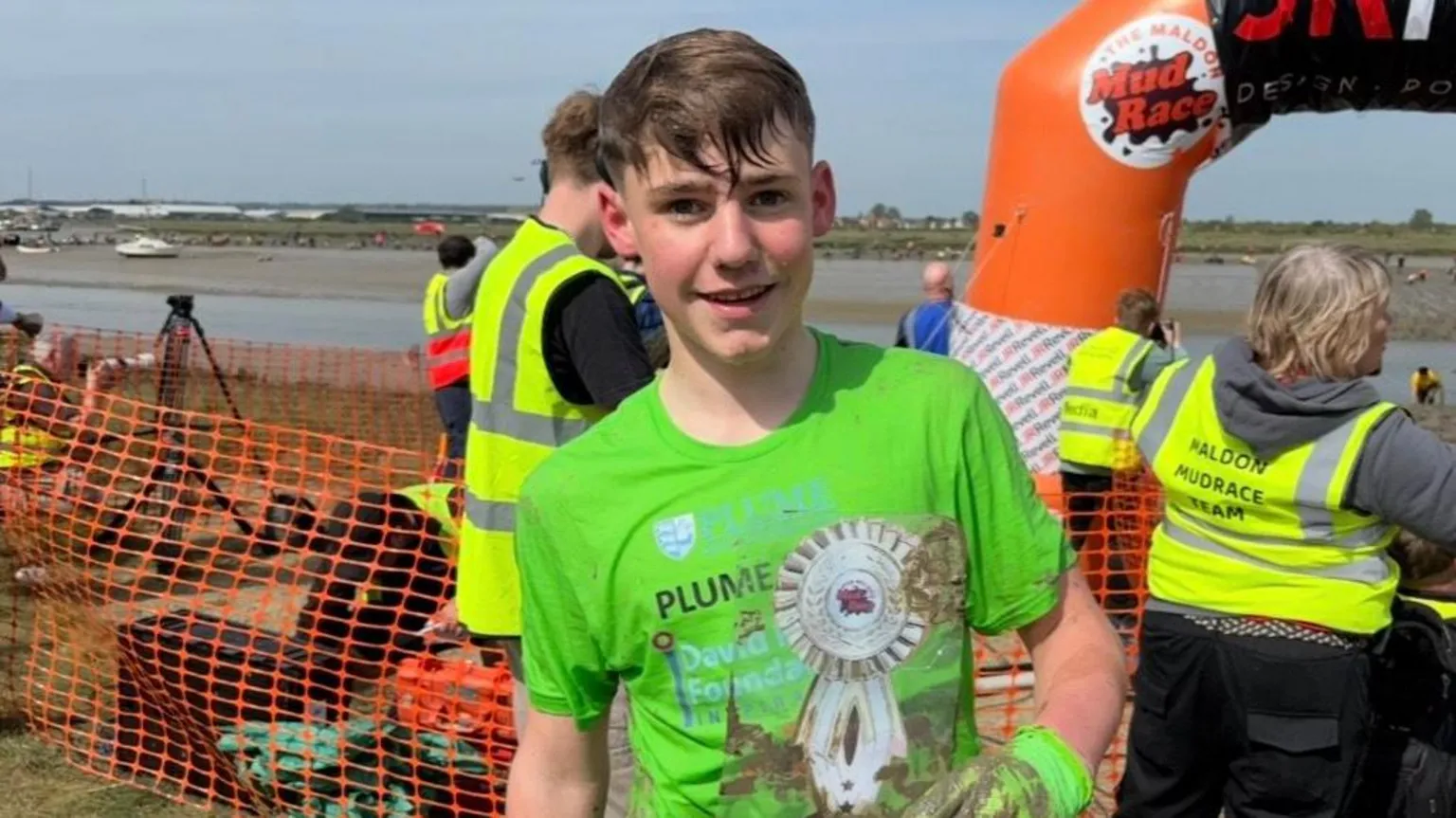 A teenage boy smiles at the camera. He has wet hair and wears a bright green top and green gloves.