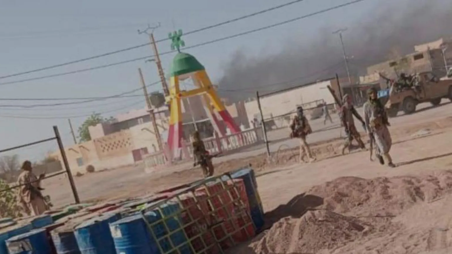 Azawad Liberation Front via AP Grainy image of five fighters spaced out and standing in a sandy setting. There are structures in the background. In the foreground there is a crate of barrels.