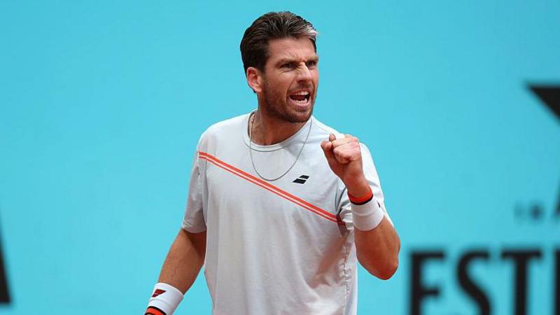 Cameron Norrie is wearing a white t-shirt with an orange sash and holding up his fist