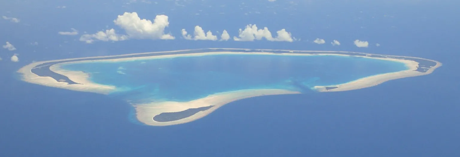 Simon Diffey A photo taken out of a plane showing the atoll of Abemama. It is a narrow strip of land in the middle of the ocean curving almost into a circle with a big lagoon in the middle. 