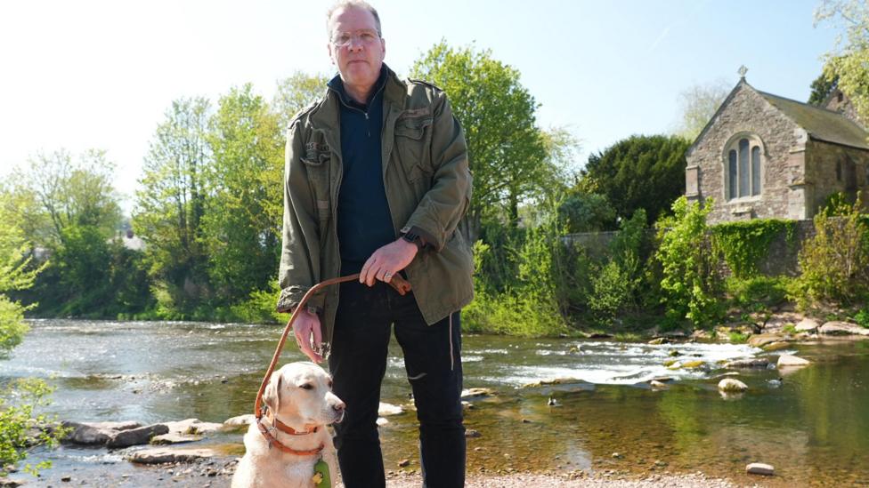 Y parafeddyg Philip Pearce a'i gi Finn ar lan yr afon yn Nhrefynwy