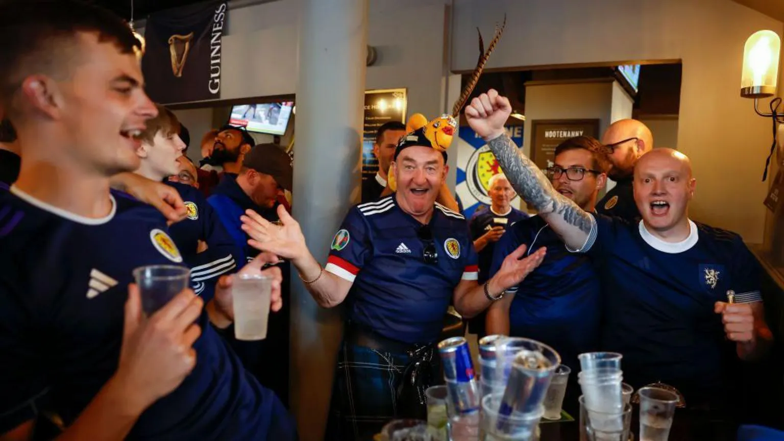  A group of Scotland fans in a pub - they are wearing kilts and replica shirts, with pint glasses sitting in front of them.