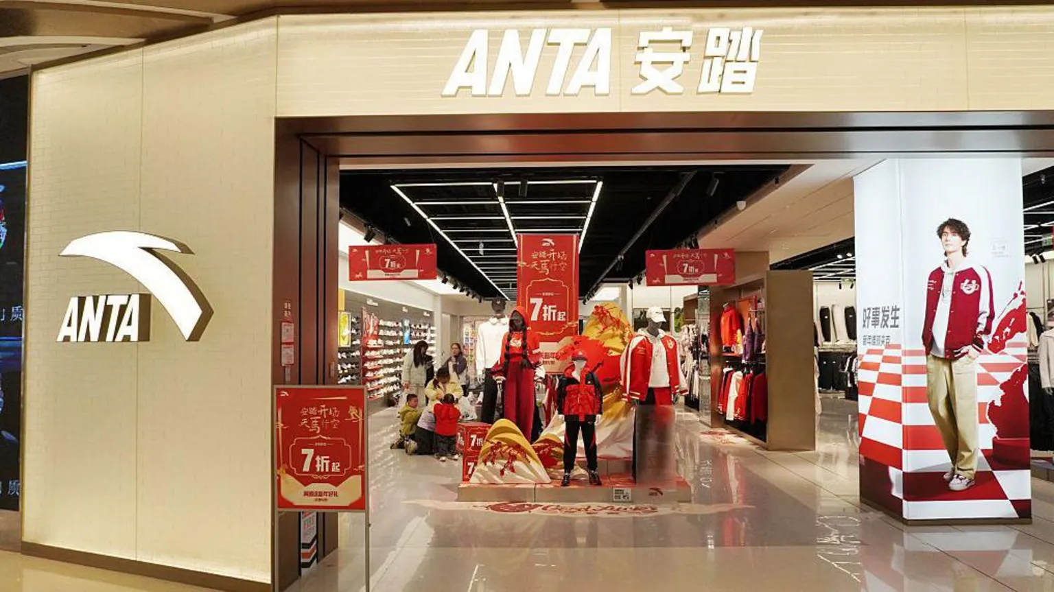  The front entrance of an Anta shop in China with multiple red banners promoting discounts.