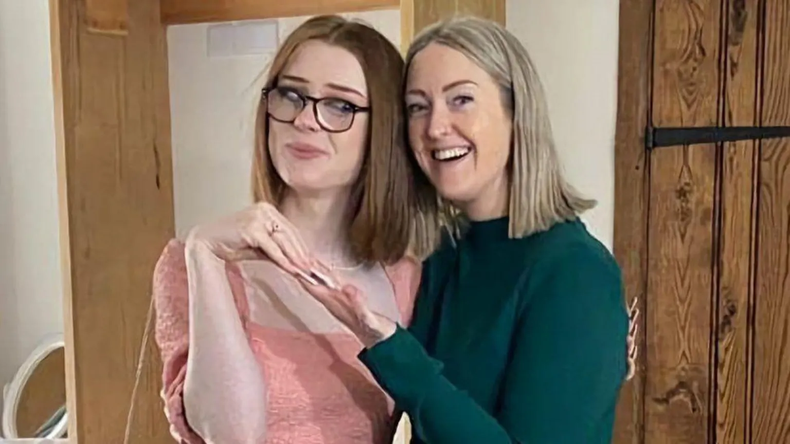 Family handout Brianna and Esther Ghey pose together with Esther holding up Brianna's hand and smiling. Esther has shoulder length blonde hair and wears a green top. Brianna wears glasses and has shoulder length red hair over a pink top.