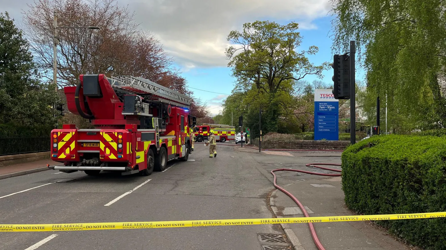 A fire engine next to a Tesco sign on a road surrounded by trees