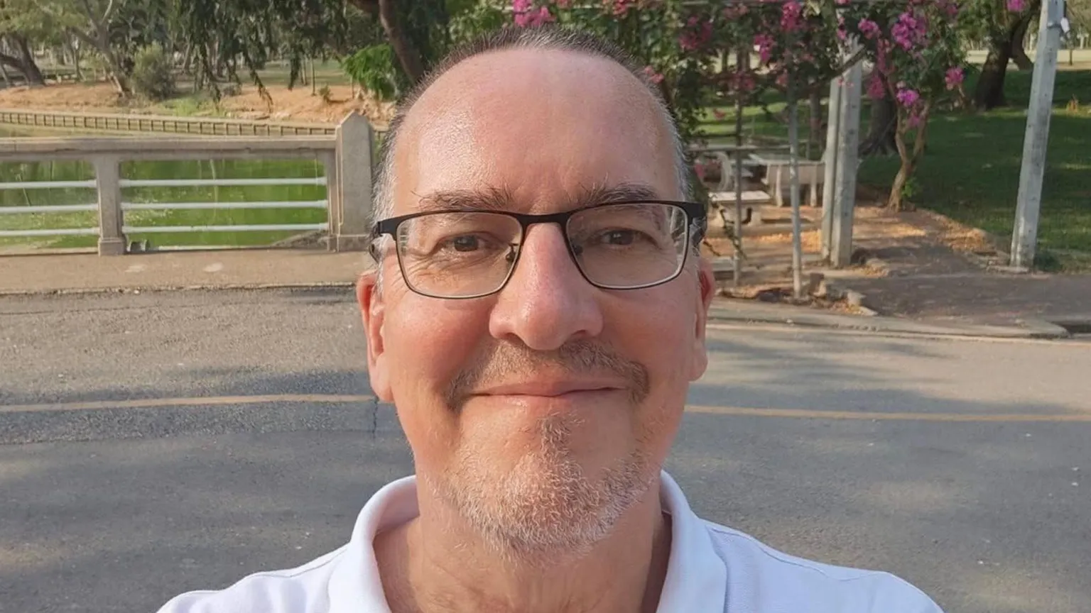 A middle-aged balding man in glasses smiles as he takes a selfie. 
