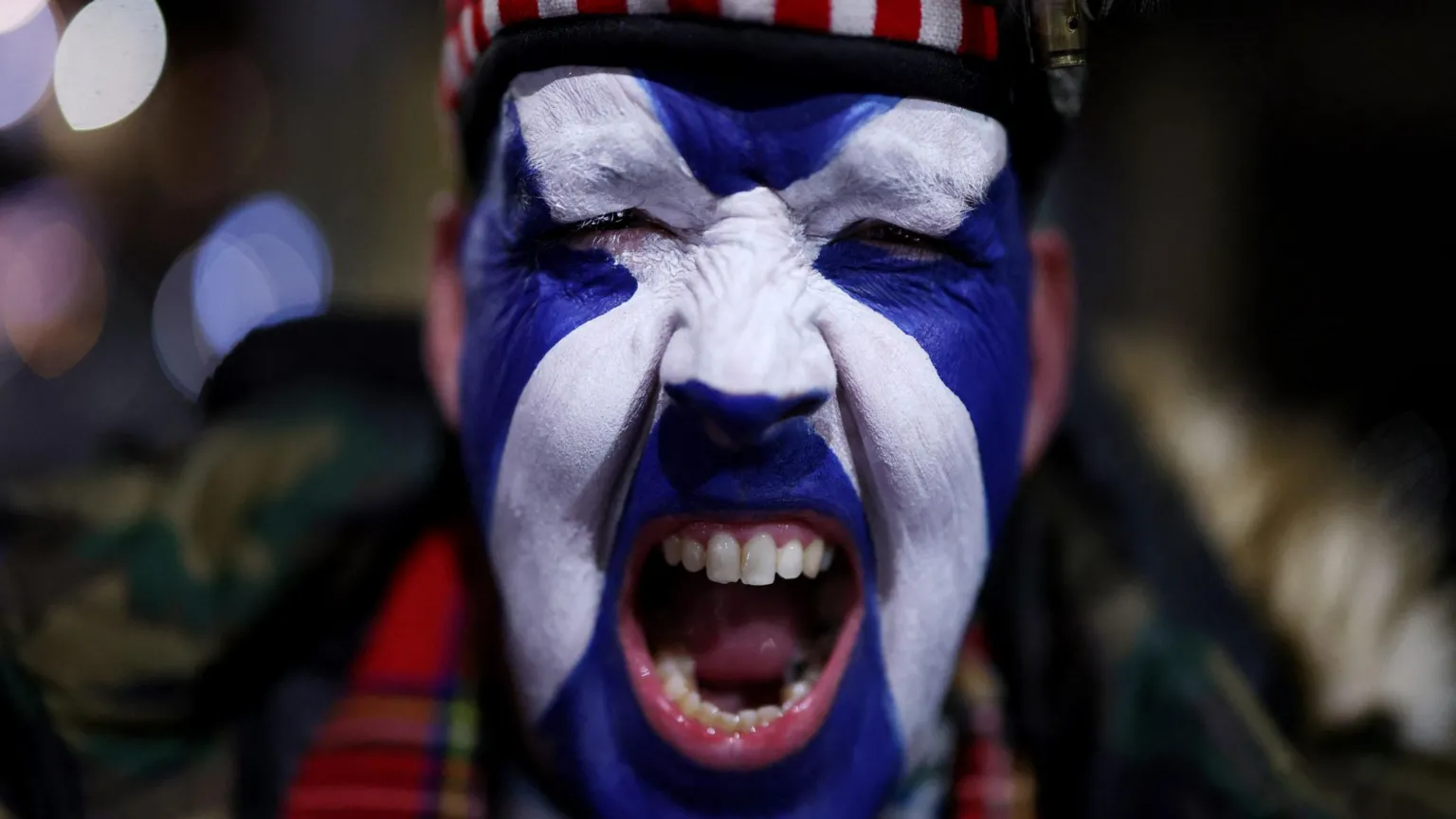  A close up of a Scotland fan who has their face painted with a Scottish saltire and is wearing a Glengarry hat.