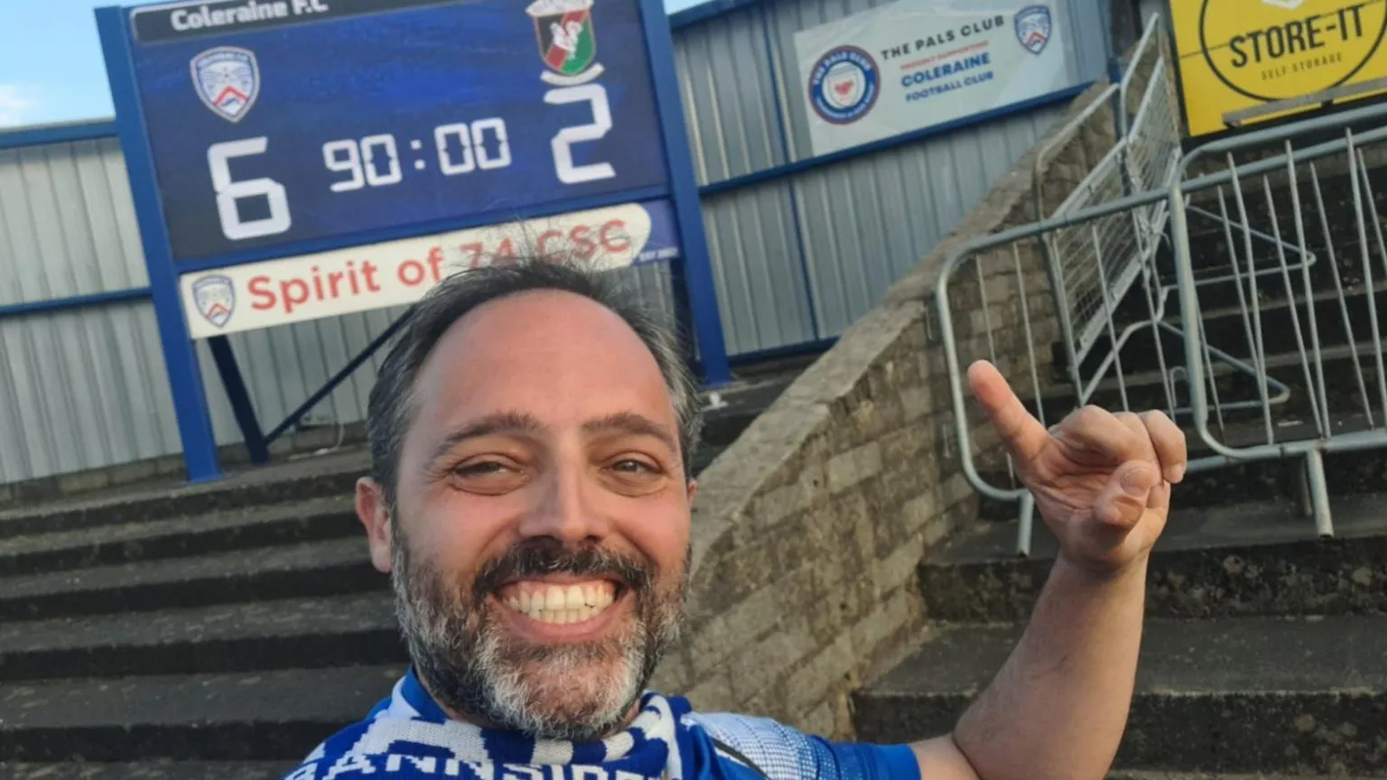 Andrea Lai A man smiling at the camera, he is wearing a blue and white scarf and top, he has dark hair and beard