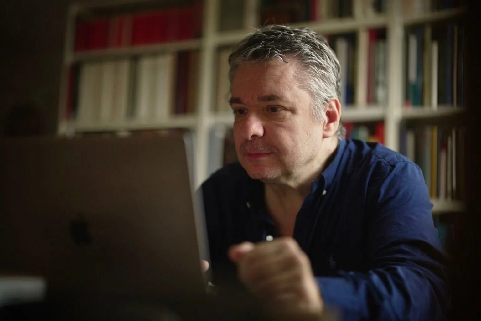 BBC/Katie Razzall Dr Gradel looking at his laptop. Wearing dark blue shirt Bookcase behind him.