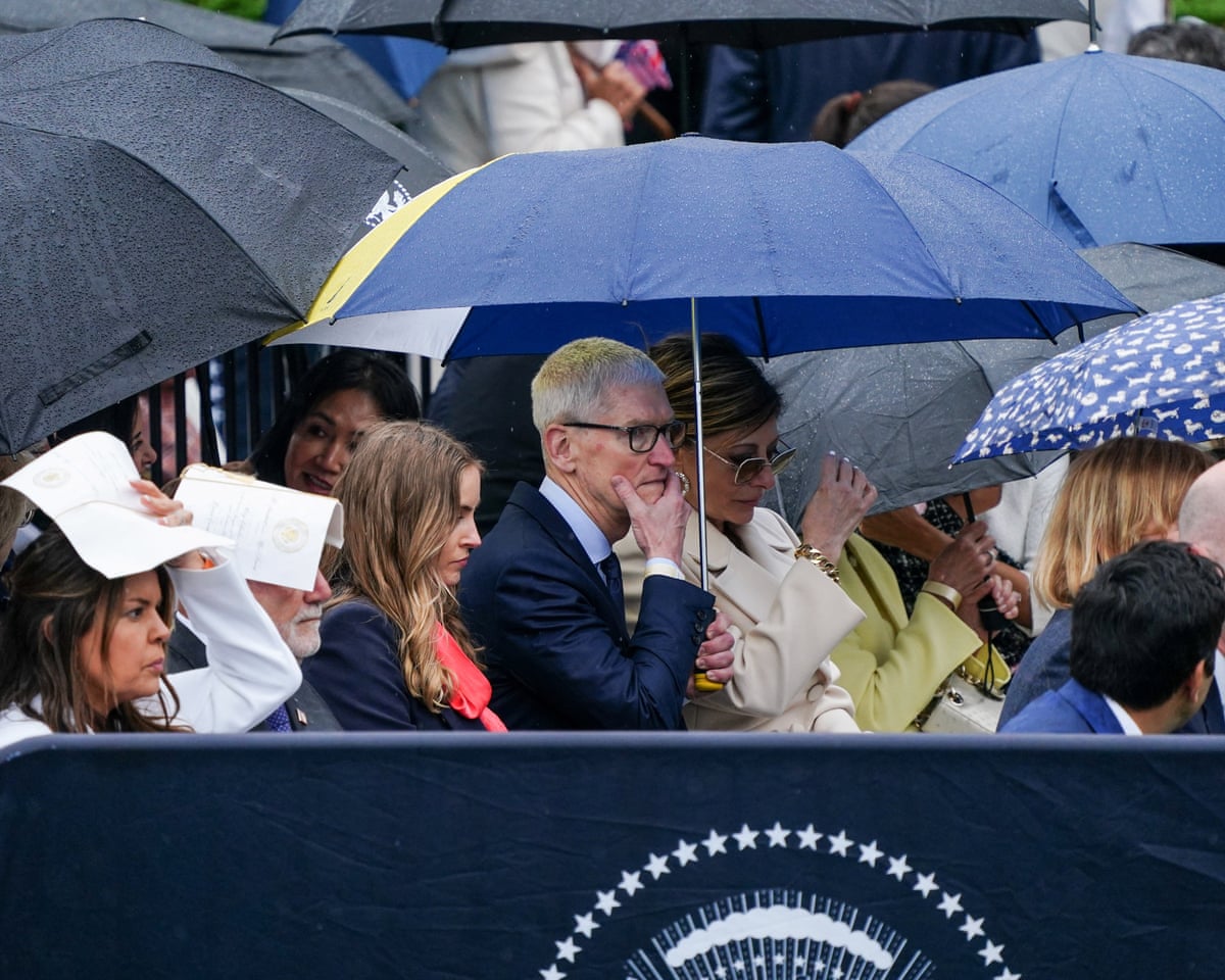 Apple CEO Tim Cook takes cover beneath an umbrella.