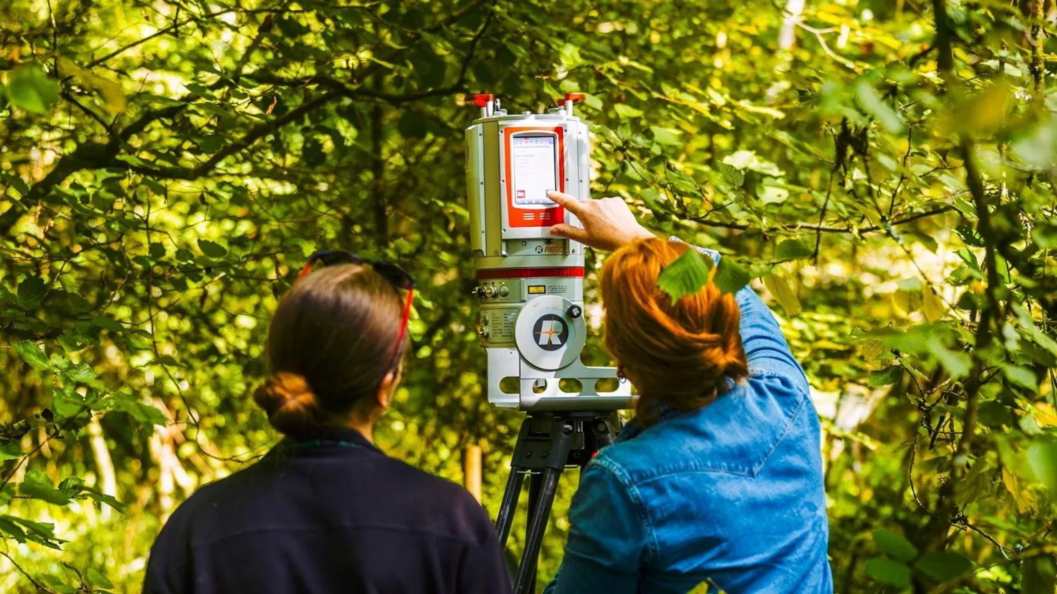 RBG Kew Two women, with their backs turned, are operating a scanner in a nature reserve.