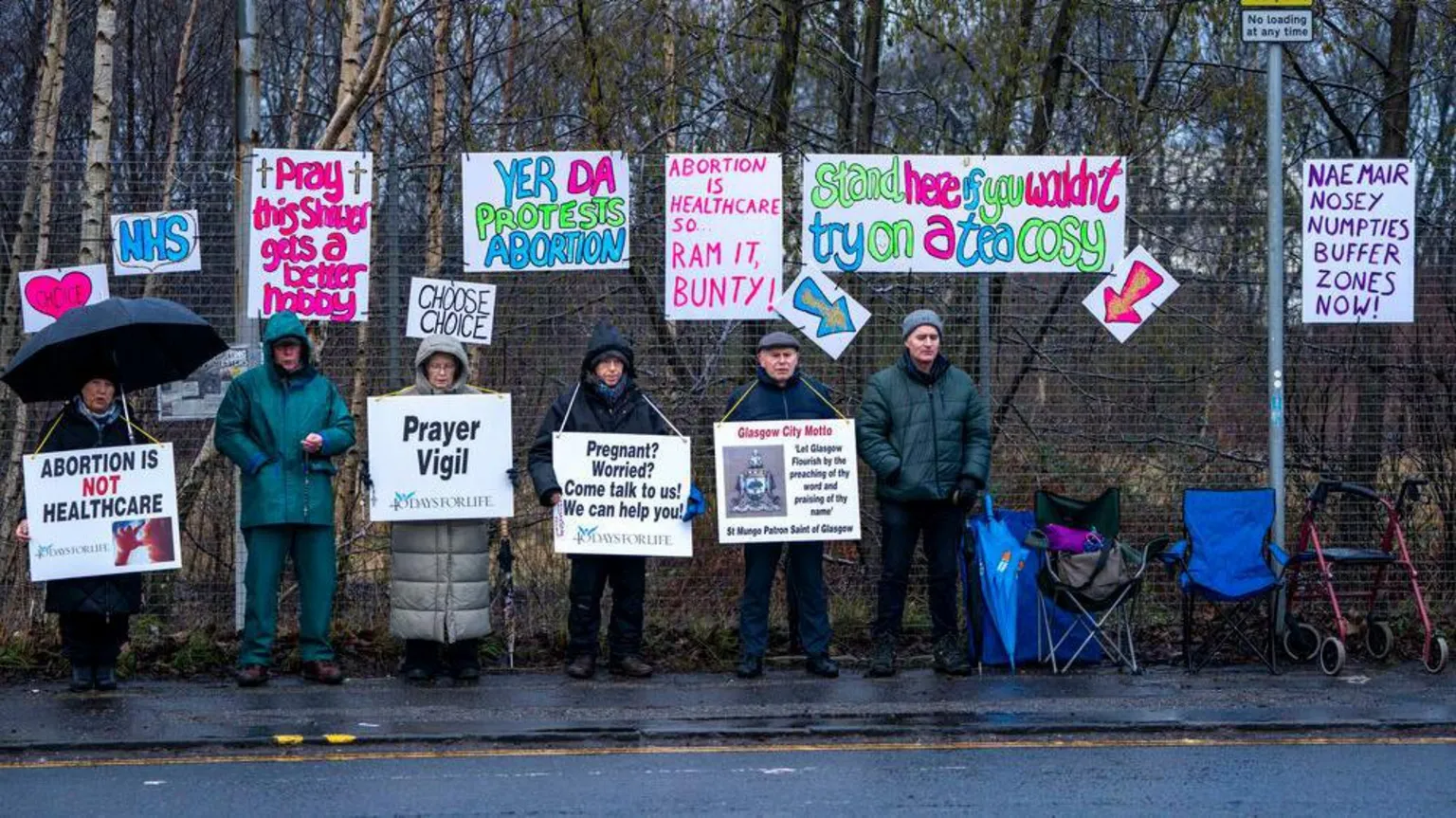  People gather by a fence holding signs saying things like 
