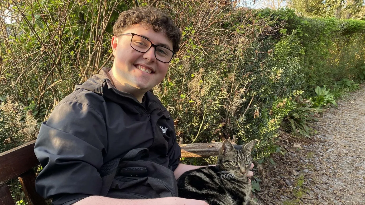 Sam Thomas A young man wearing a black top sitting on a bench in garden with a cat on his knee