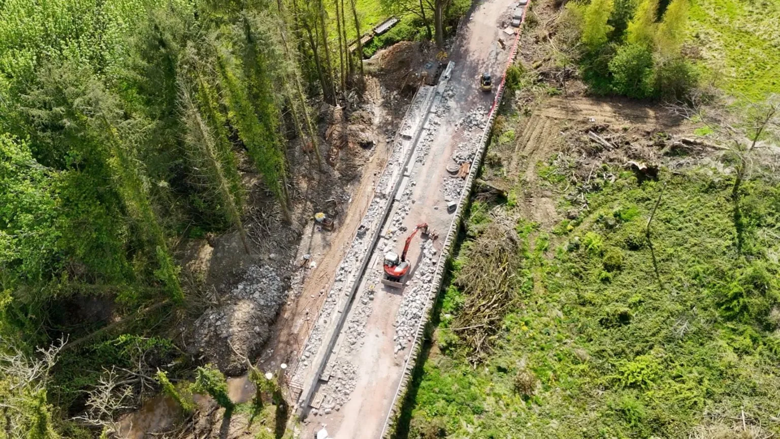 An overhead image of a bridge, with a large field on the right side of it and a row of tall trees on the left side. 