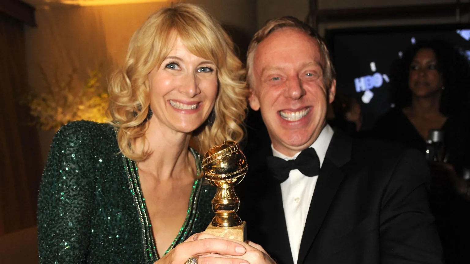  Laura Dern and Mike White in formal dress, smiling widely together and both holding the Golden Globe statuette between them