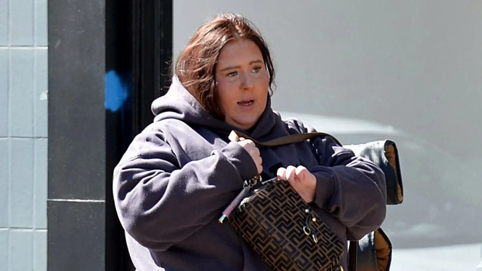 Spindrift A woman with shoulder length dark hair wearing a dark coloured hoodie and holding a handbag across her chest