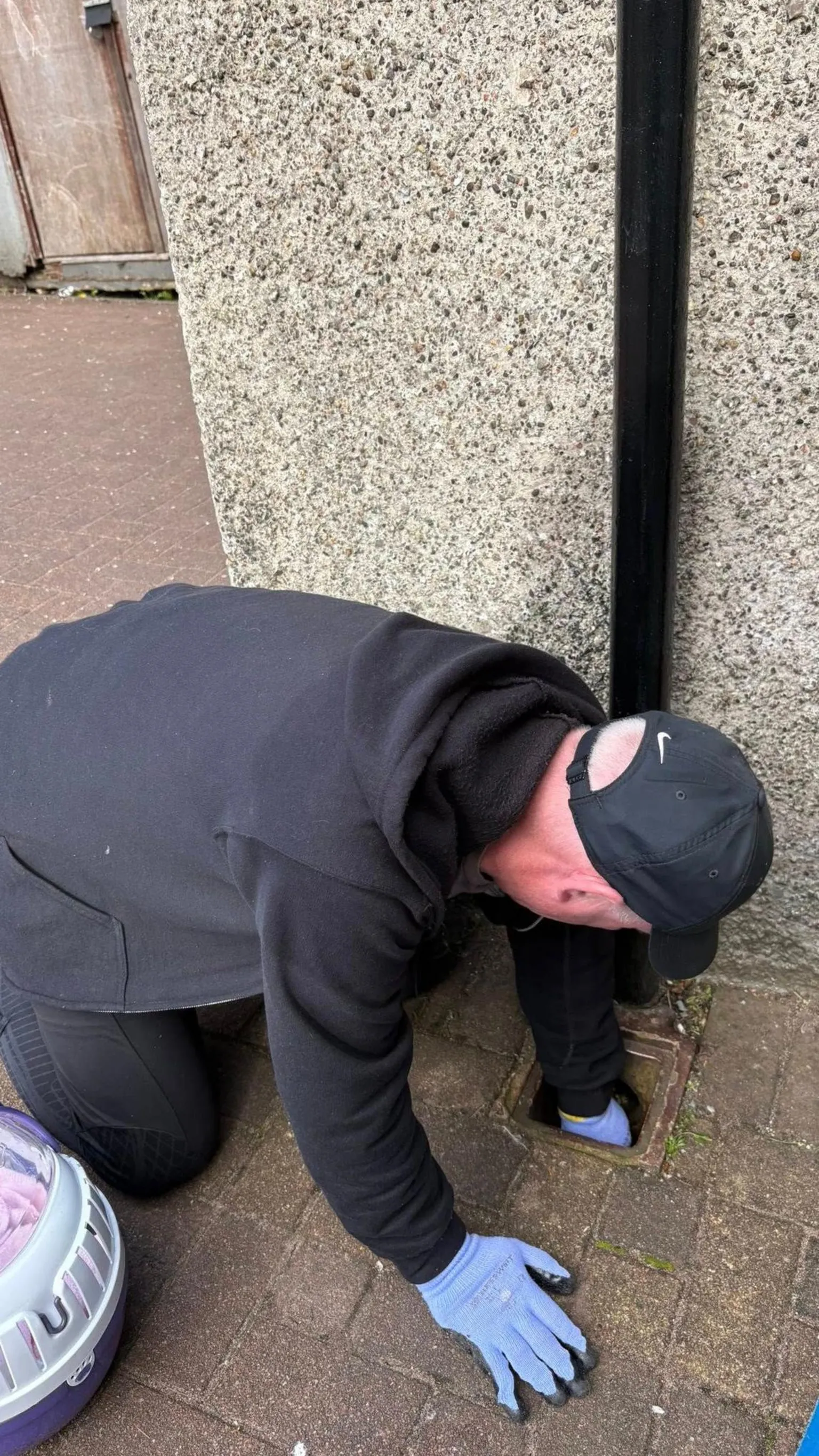 Burntisland Hedgehog Haven A man wearing thick gloves kneels on the ground next to a pipe