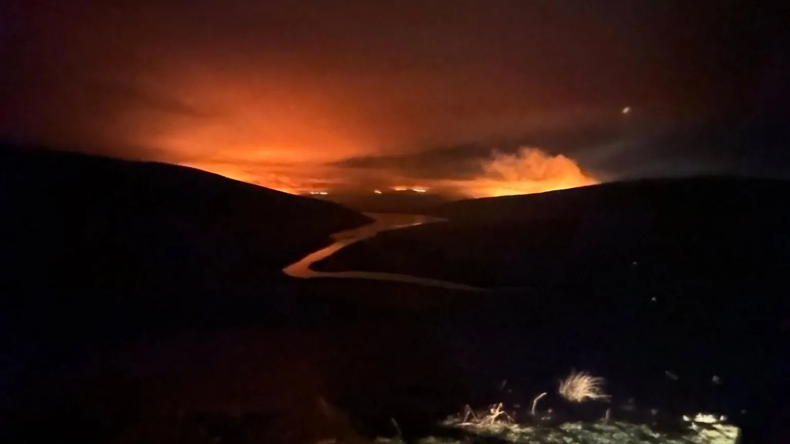 MWWFRS Rhayader Wildfires in a valley are pictured at a distance lighting up the night sky with an orange glow.