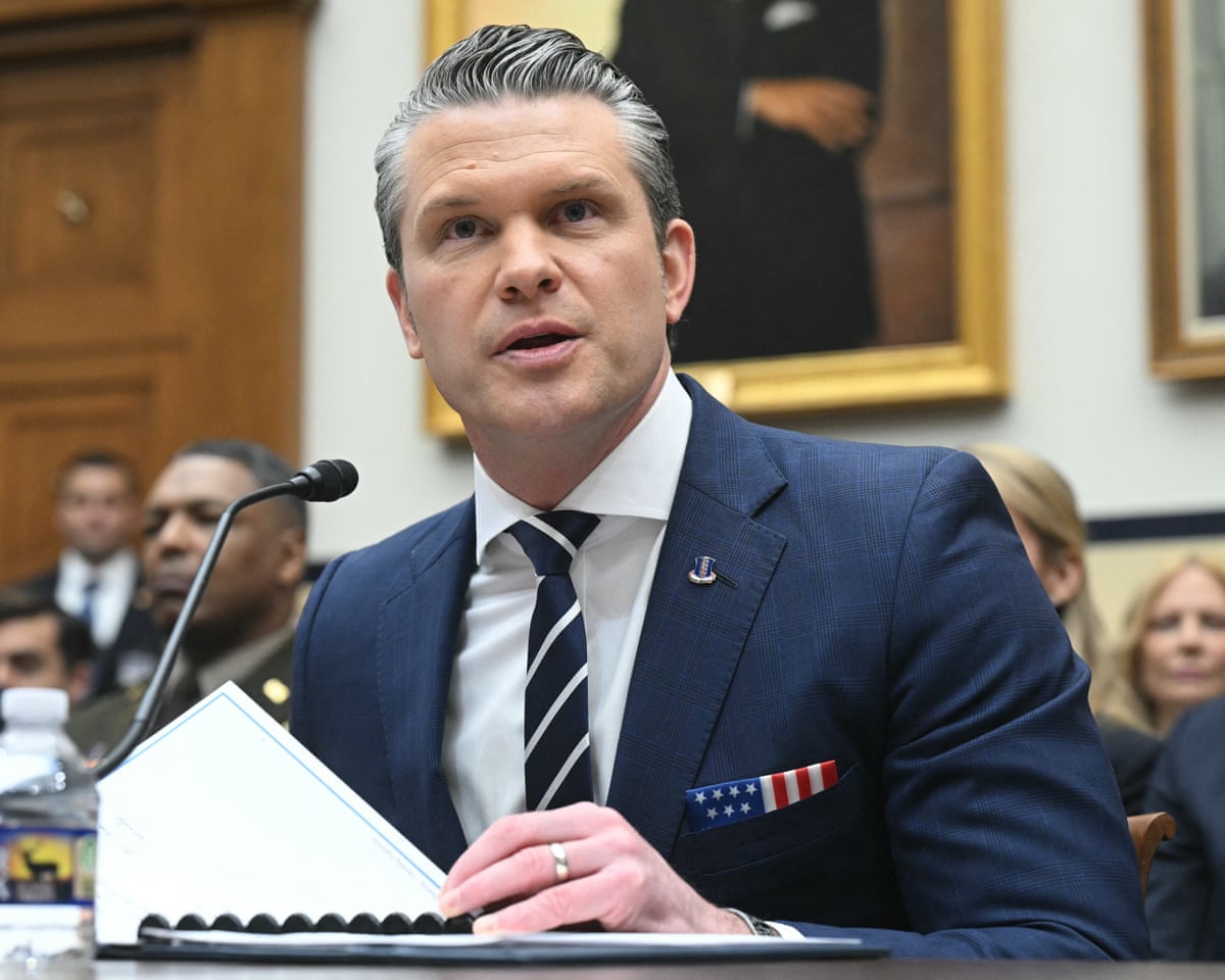 Pete Hegseth speaking into a microphone and flipping a page in his notebook.