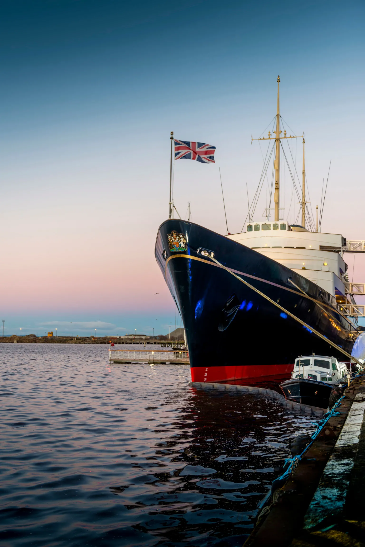 Tony Marsh A large boat sits in the water with the sun setting behind it. The boat is red, black and white and has a Union Jack flying on a flag pole on the front.