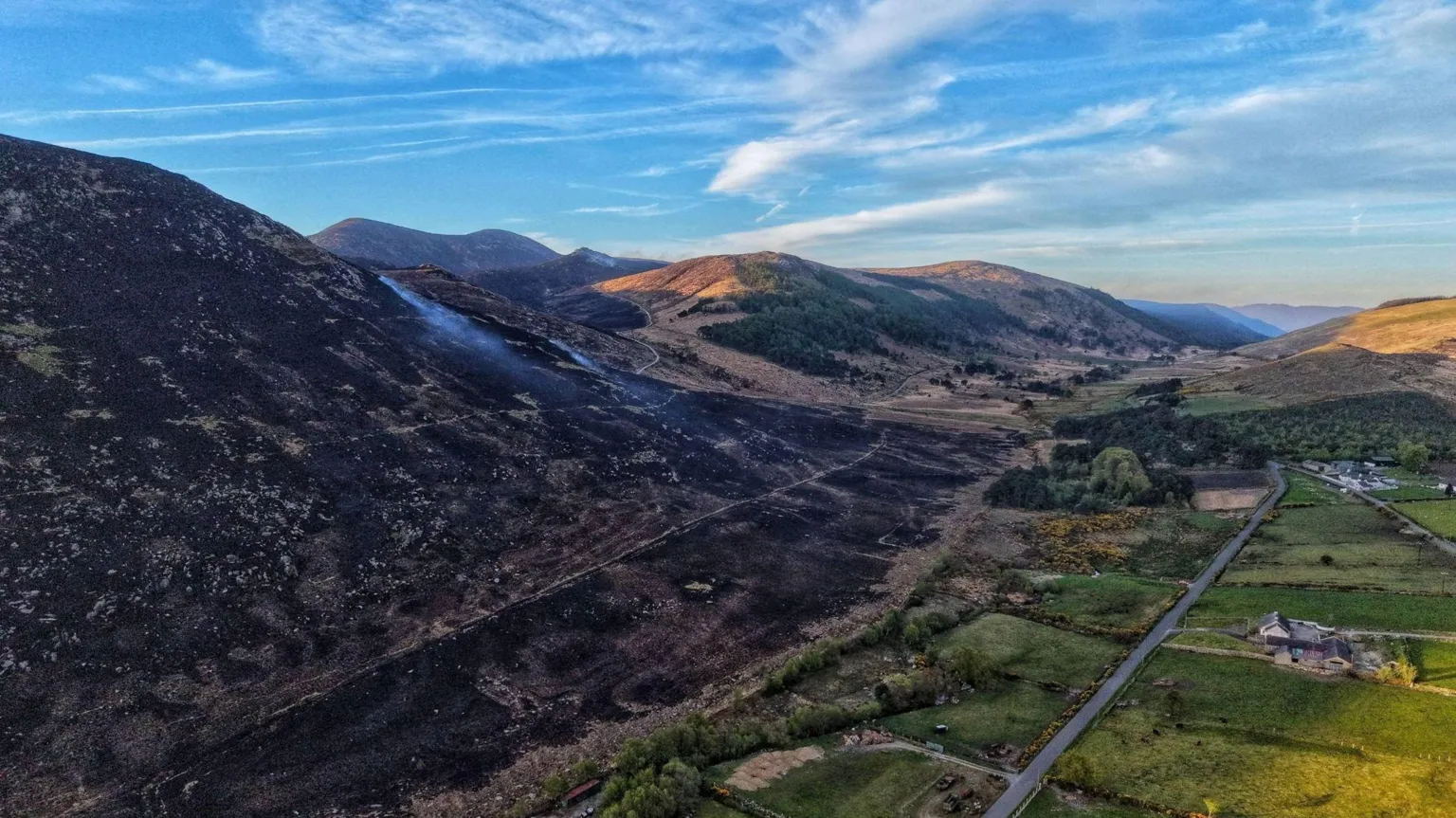 SKY-Ranger NI An aerial shot showing an areas of the Mourne Mountains which has been burnt. The area is black, in contrast with greenery further away. A house can be seen away from the burnt area.