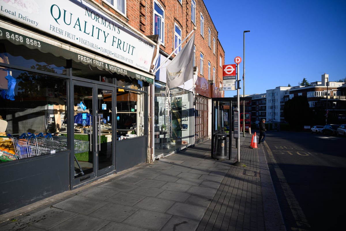 A view of a bus stop outside shops. 