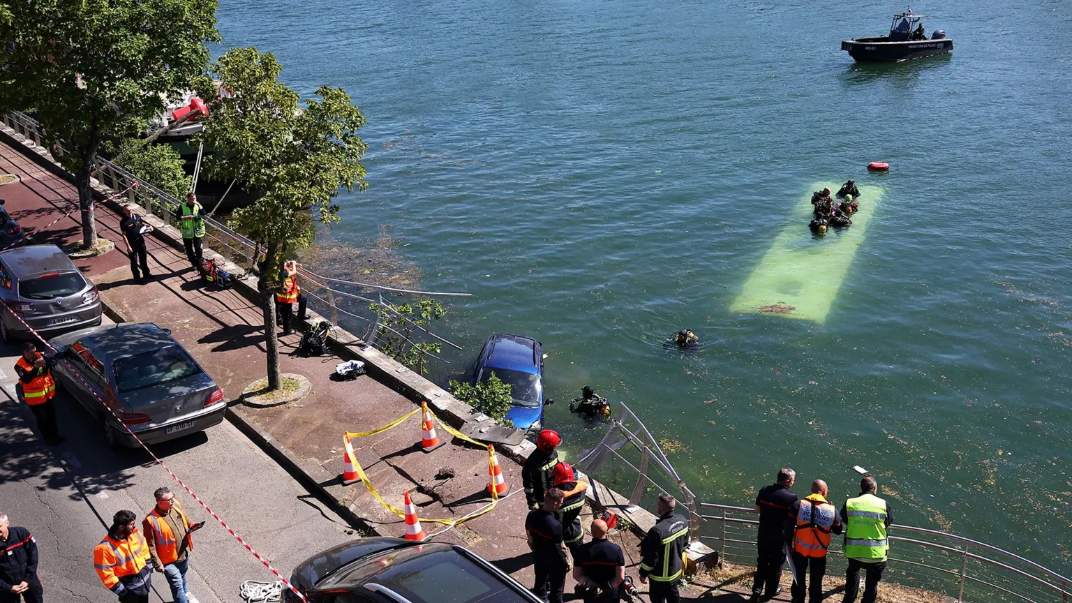  A view of the bus under water from the street, where several people in high-vis jackets are stood and cordons and traffic cones have been set out.