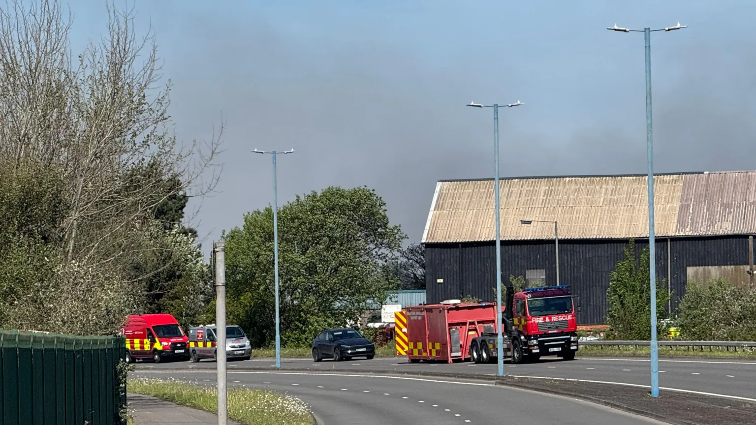 the same building with three fire emergency vehicles parked on an empty two carriage motorway in front 