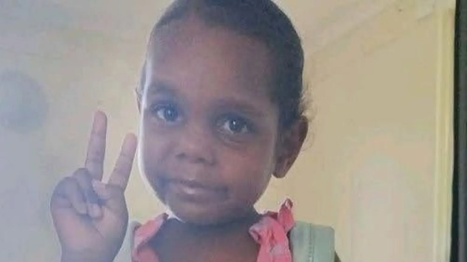 Northern Territory Police An girl wearing a pink dress and blue backpack poses for a picture, holding up the peace sign