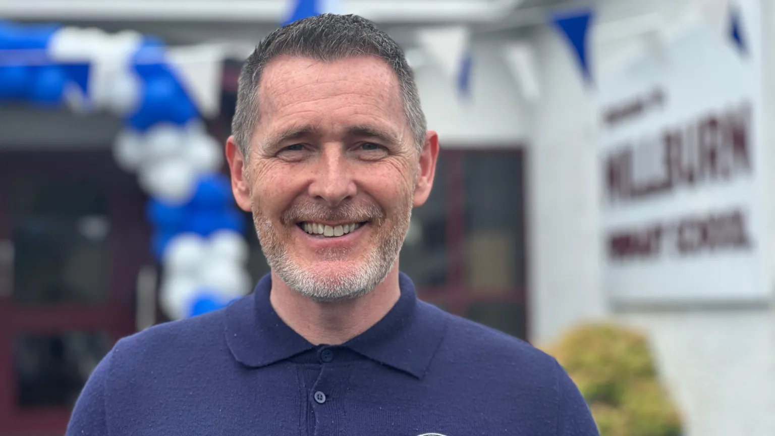 Jamie Selfridge is a middle aged man with greying dark brown hair and a short grey beard. He is smiling at the camera and is wearing a dark blue polo shirt