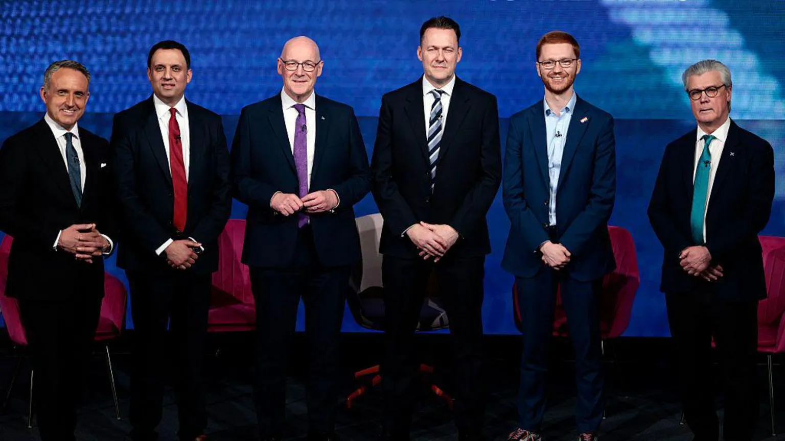  The leaders of Scotland's six largest political parties standing in a row - from left, Alex Cole-Hamilton, a man with greying hair in a dark suit and tie, Anas Sarwar, a man with black hair in a dark suit and red tie, John Swinney, a bald man with glasses in a dark suit and purple tie, Russell Findlay, a man with black hair in a dark suit and stripy blue tie, Ross Greer, a man with red hair and glasses in a dark suit with no tie, and Malcolm Offord, a man with grey hair and glasses wearing a dark suit with an aquamarine tie.