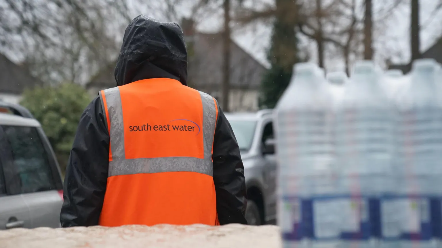 A person in an orange jacket. Behind them are some water bottles. 