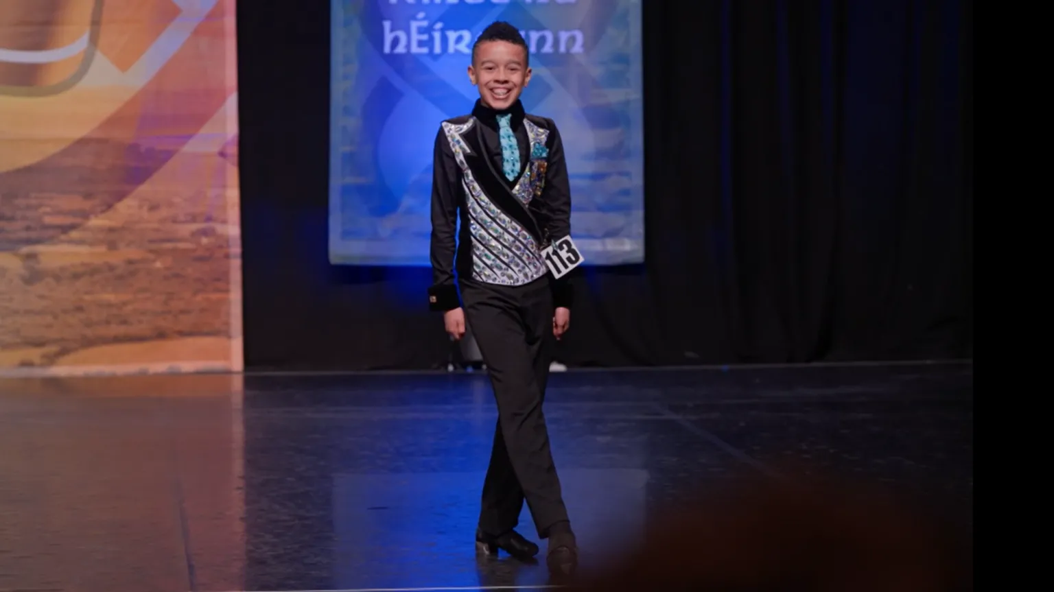 HopSkip Productions A young boy wearing a waistcoat and black trousers, legs crossed dancing, he is smiling on stage