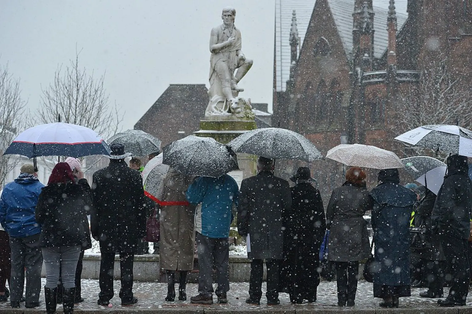  A statue of Robert Burns in Dumfries on a snowy day with lots of people with umbrellas