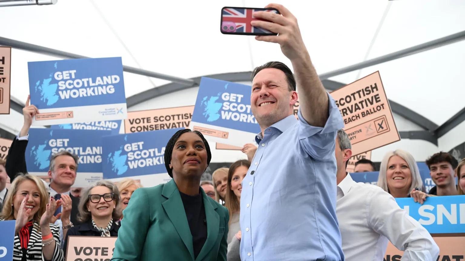  Russell Findlay takes a selfie with Kemi Badenoch at a campaign event. There are activists behind them holding posters.