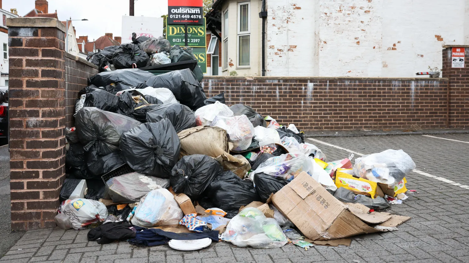 EPA/Shutterstock A large pile of rubbish in a small private parking area on a suburban street. Black and white bin bags have spilled open, with soiled flattened carboard and other detritus on the floor. Homes and for sale signs can be seen behind.