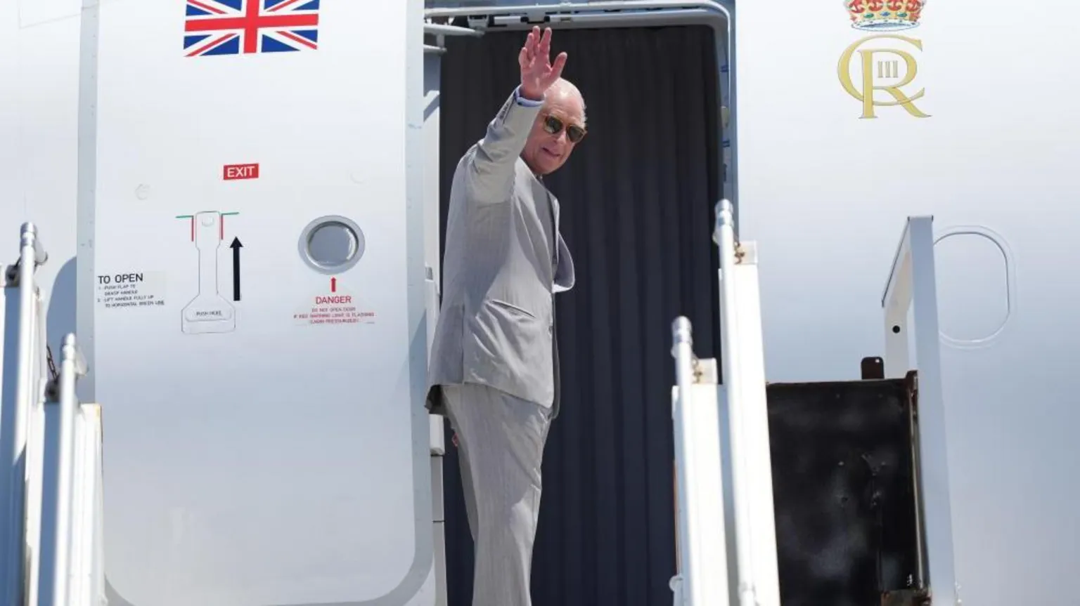  The King boards a plane with the Union Jack and turns to wave. He wears sunglasses.