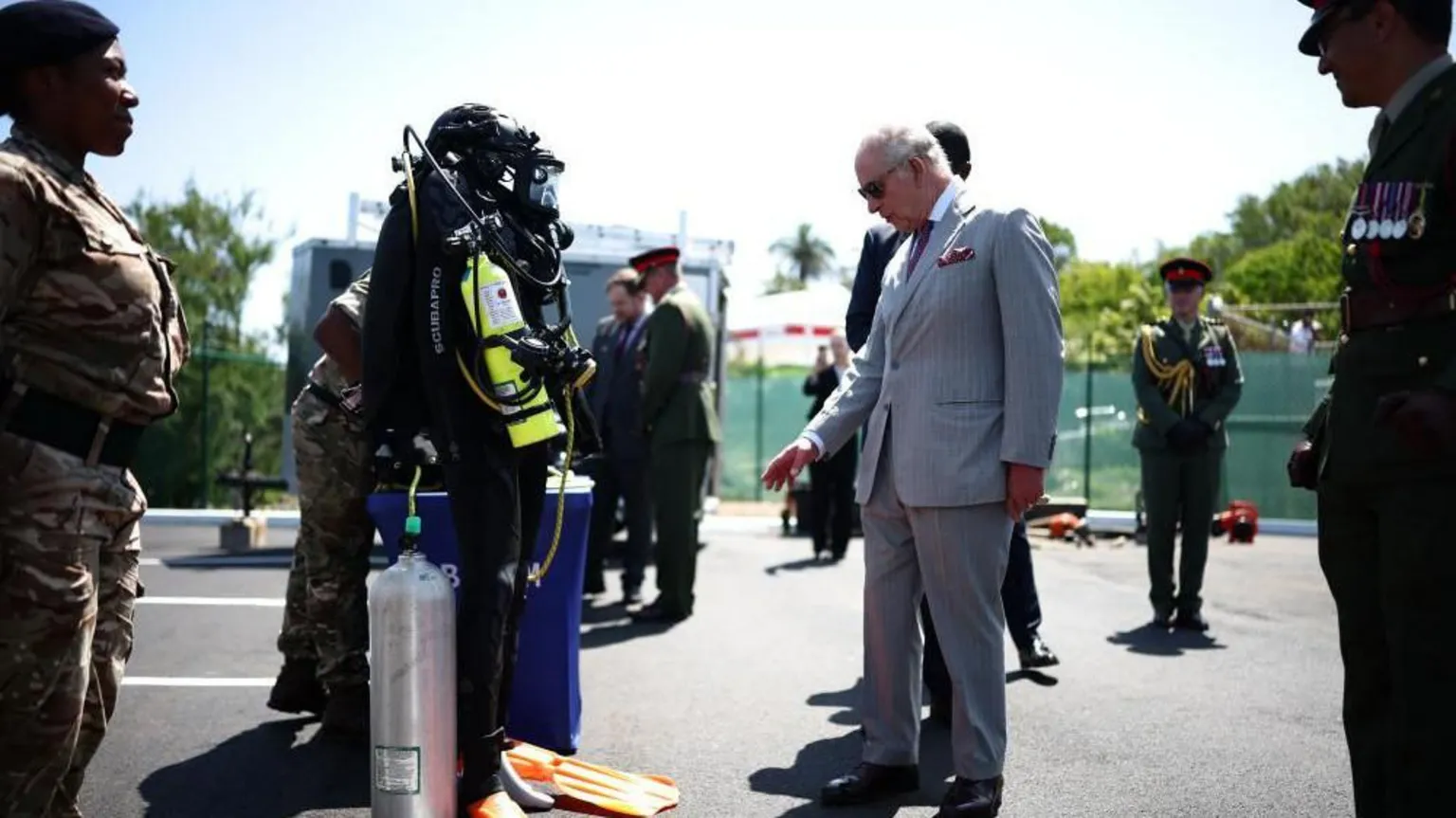  The King wearing a suit gestures towards equipment that is being demonstrated by the Royal Bermuda Regiment Coast Guard