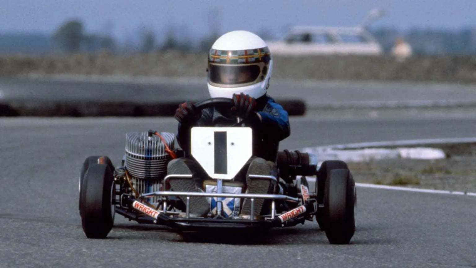  A young Allan McNish in a racing kart with the number 1 on the front. He has a white helmet on with a tartan trim.