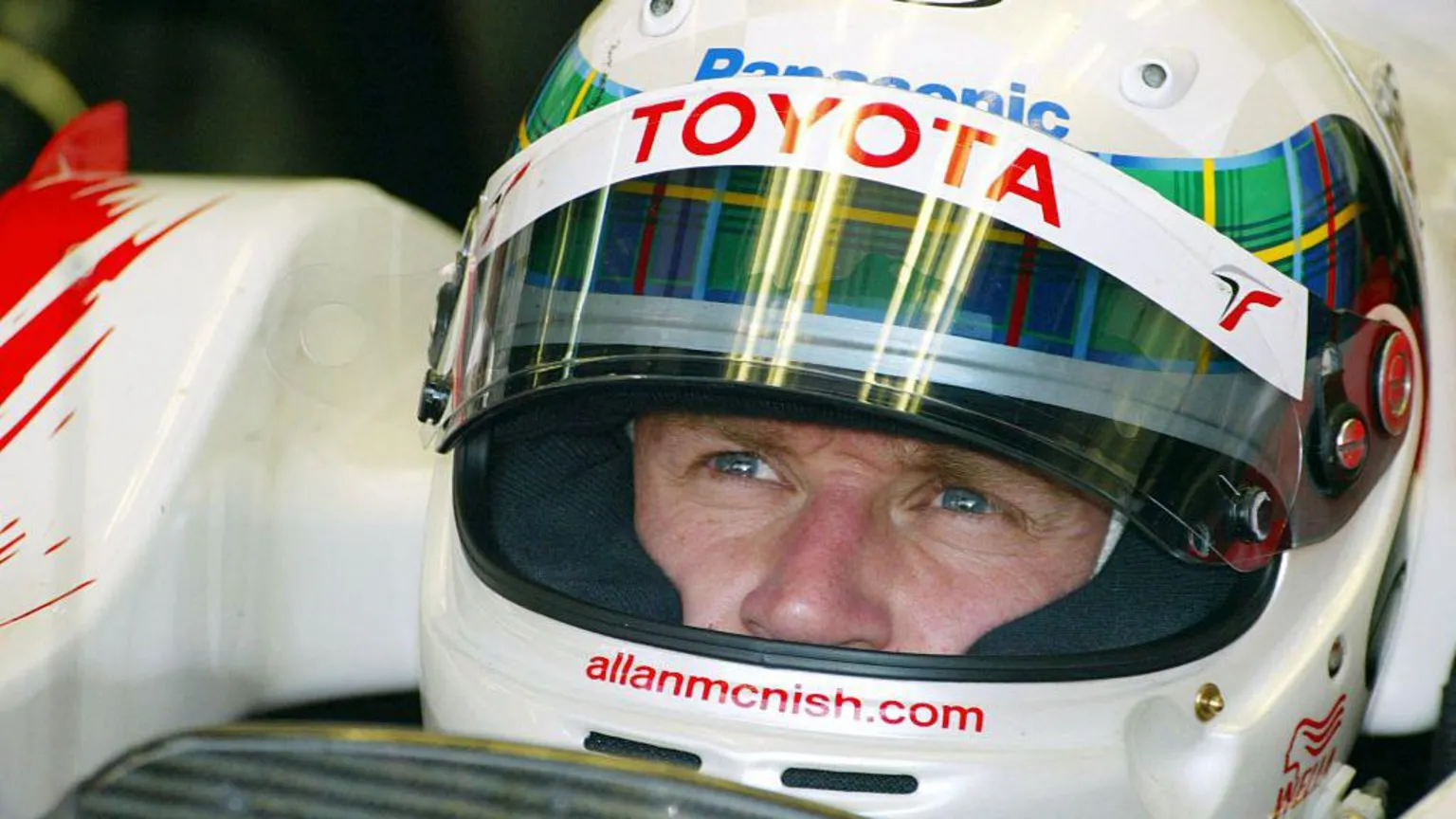  Allan McNish in close up with a Toyota helmet on and tartan trim round it
