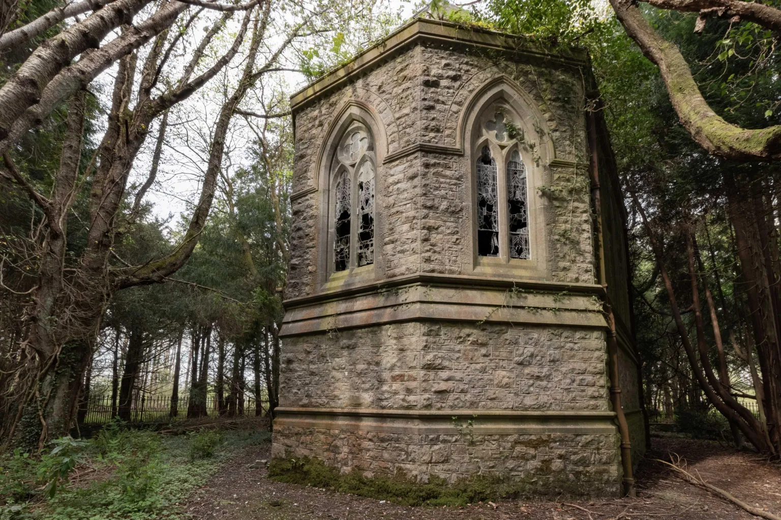 Dan Weatherley This image shows a Victorian era building, its located in the woods and surrounded by trees. The building has two smashed stained glass windows. 