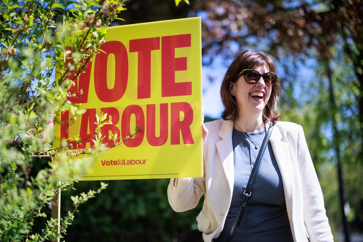 Lucy Powell smiles next to a flag that reads: ‘Vote Labour’